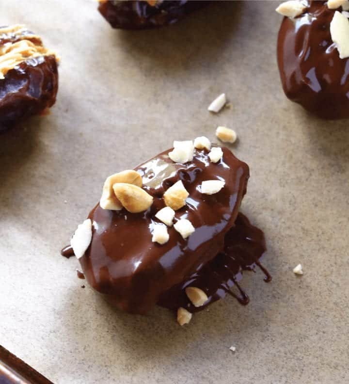 healthy homemade snickers step 4- freeze snicker dates to set chocolate chocolate covered date with peanuts on top on parchment paper #chocolatedates #chocolatecoveredates #nobakedessert #chocolatecoveredsnickerdates