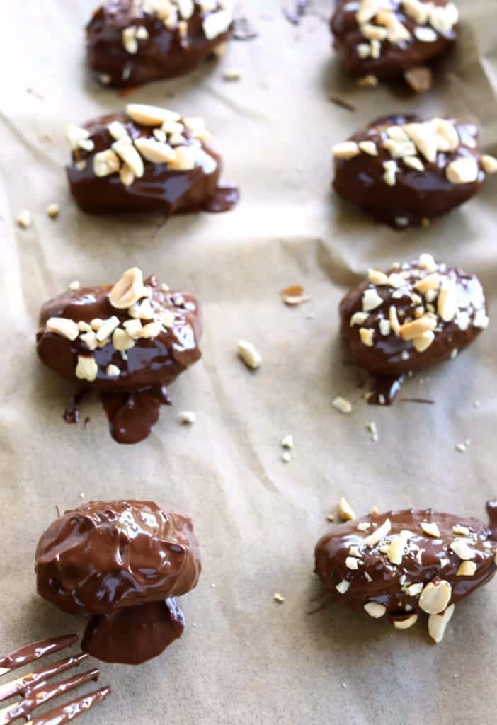healthy homemade snickers step 3- top chocolate stuffed dates with chopped peanuts melted chocolate on parchment paper #snickerdates #healthysnickers #chocolate #dessert #chocolatecovereddates #homemadesnickers #chocolatecoveredsnickerdates #healthydessert