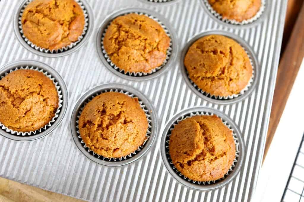 overhead picture of fresh baked pumpkin muffins in corregated muffin tin on wood cutting board