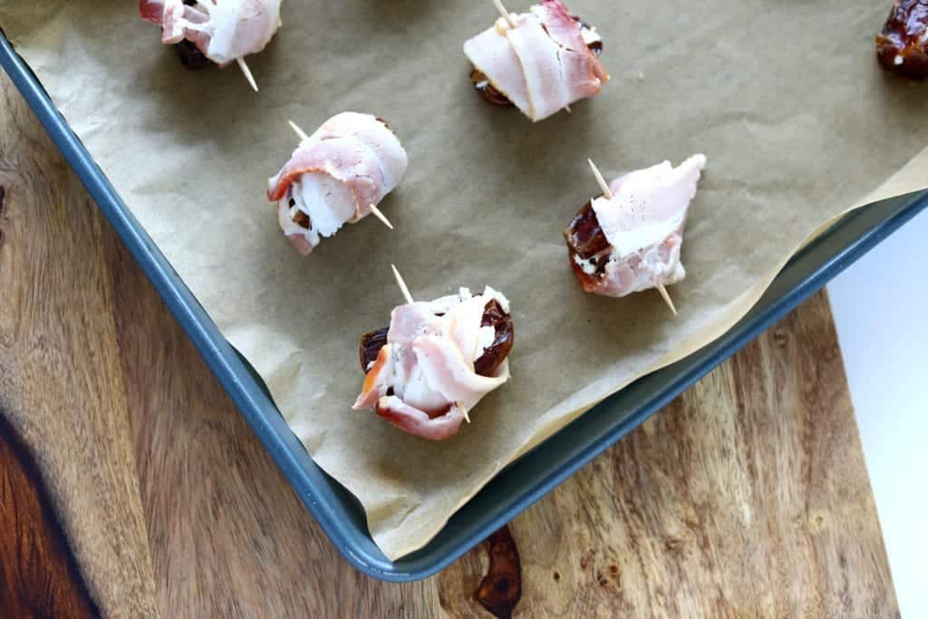 Overhead picture of prepared bacon wrapped dates with toothpick on pan with parchment paper ready to bake #bingeworthybites #baconwrappeddateswithcheese #baconwrappeddates #thanksgivingappetizers #appetizers #partyappetizers 