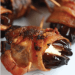 Close up of bacon wrapped dates stuffed with cream cheese on a white plate ready to serve #bingeworthybites #baconwrappeddateswithcheese #baconwrappeddates #thanksgivingappetizers #appetizers #partyappetizers