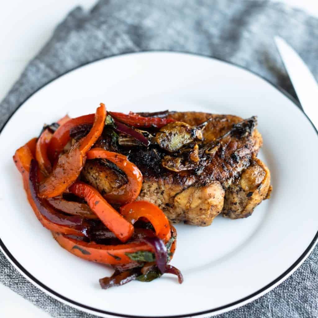 Gordon Ramsay's Pork Chops with Peppers beautifully sautéed pork chop and sweet and sour peppers with red onions basil and garlic (peppers and onions served on the side). Plated on a white dish with black rim and denim napkin #porkchops #homecooking #recipe #dinner #easyrecipes #gordonramsayrecipes #gordonramsayporkchop #porkchop #peppers #sweetandsourpeppers #gordonramsay #cookbookreview #bestcookbooks