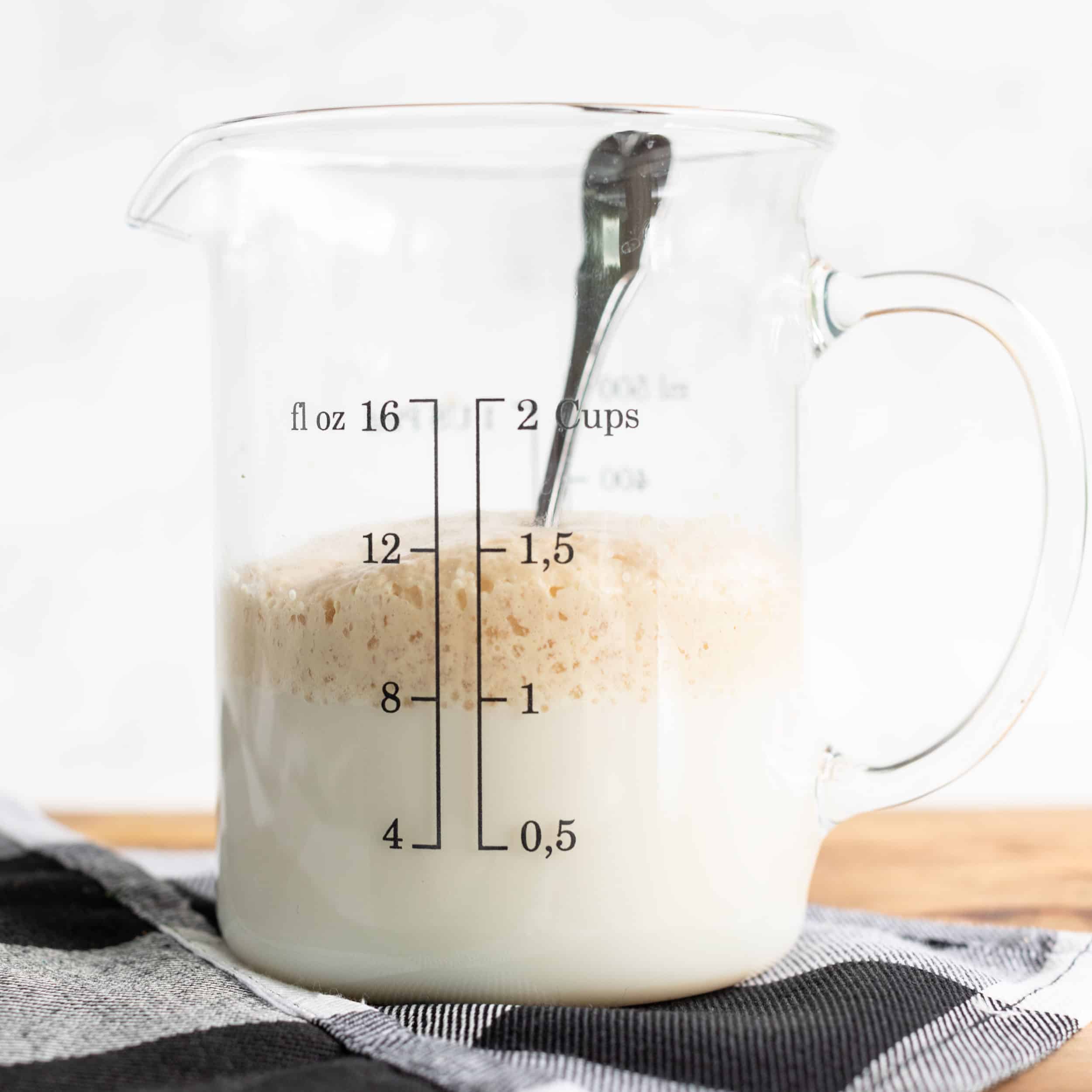 ½ cup of fat free milk and ½ cup of water with 2 ¼ teaspoon of active dry yeast and 1 tablespoon of sugar. Up close picture of measuring cup showing a picture of dissolved activated yeast for Hawaiian sweet rolls