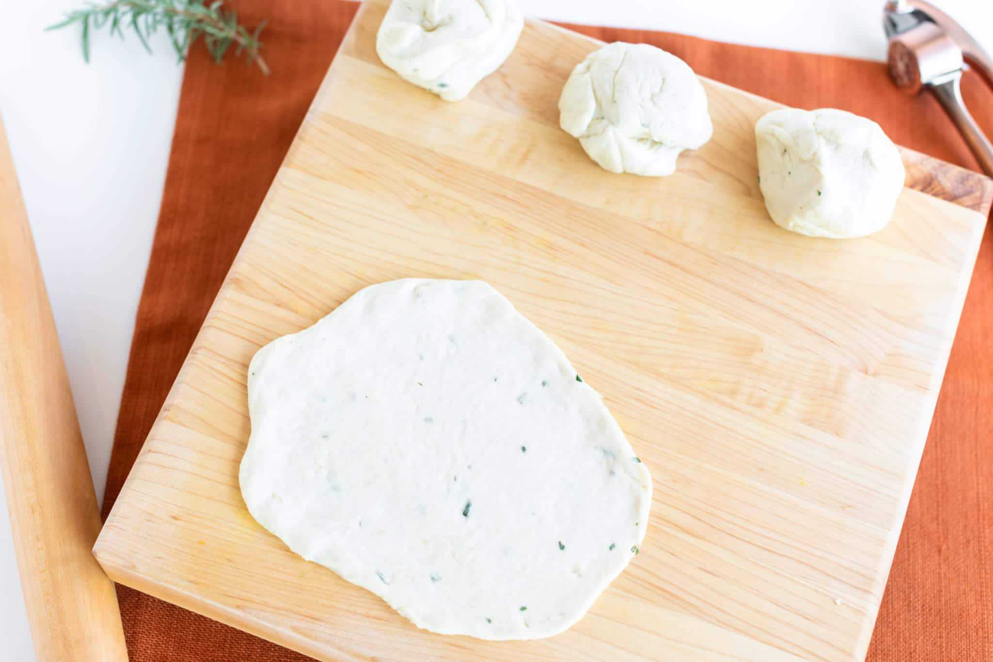 Soft Garlic Herb Naan Bread dough rolled out and portioned on chopping block 