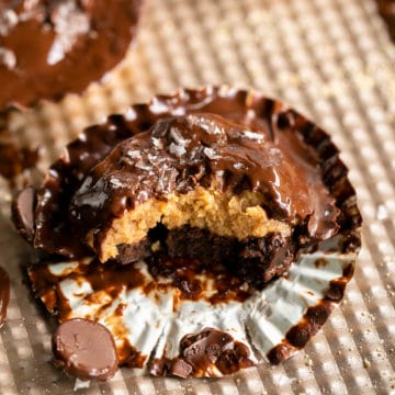 Peanut Butter Brownie Cup up close in a cupcake liner with gooey melted chocolate and 1 bite missing so you can see peanut butter brownie layers.