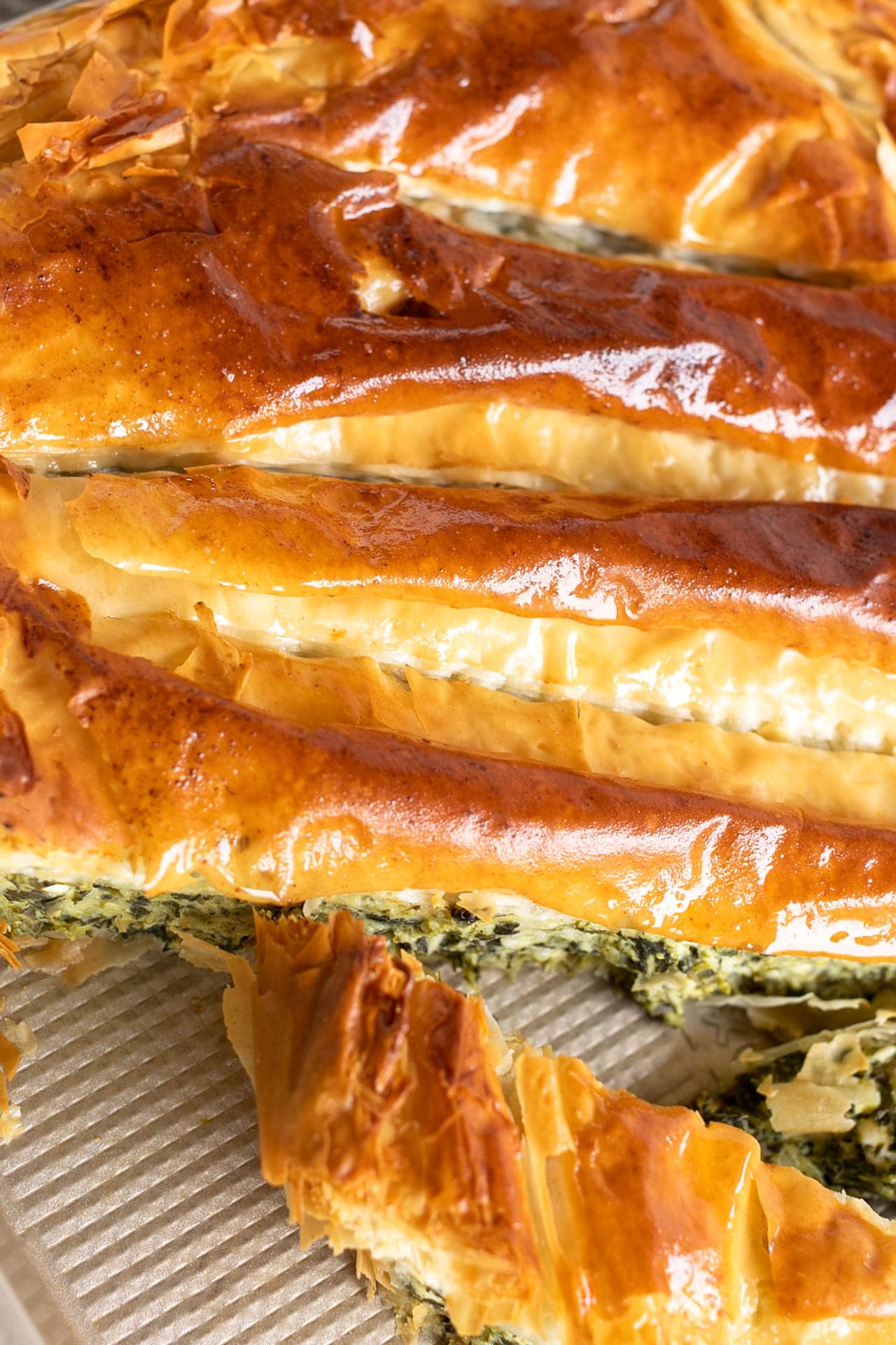 Spanakopita (Greek Spinach and Feta Pie) fresh out of the oven and sliced on an angle on a gold corrugated jelly roll baking sheet.