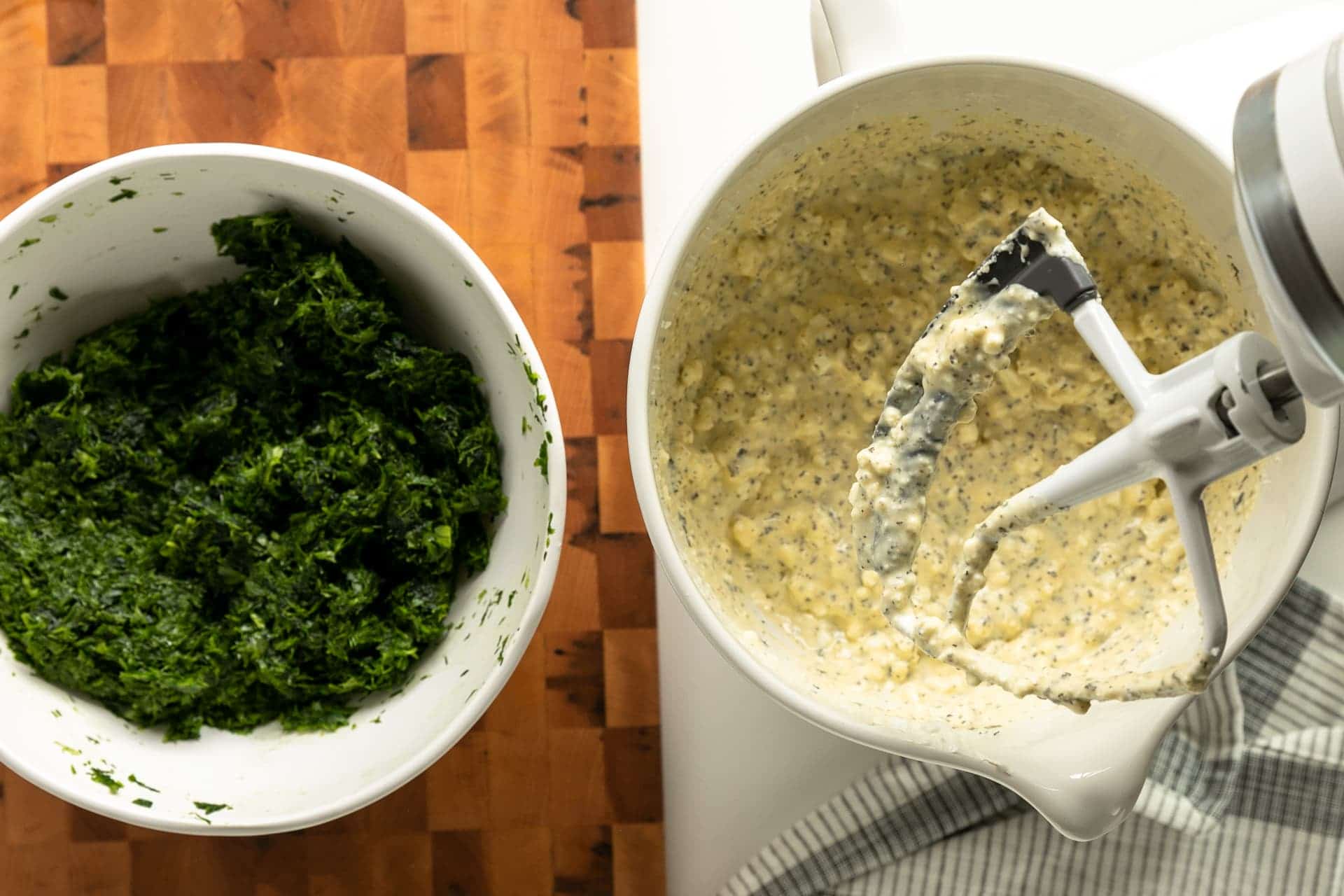 Overhead shot of spanakopita filling's wet ingredients and fresh ingredients. On the right side is a mixture of different types of cheese, egg, and seasonings. The right side chopped greens (green onion, dill, and spinach).