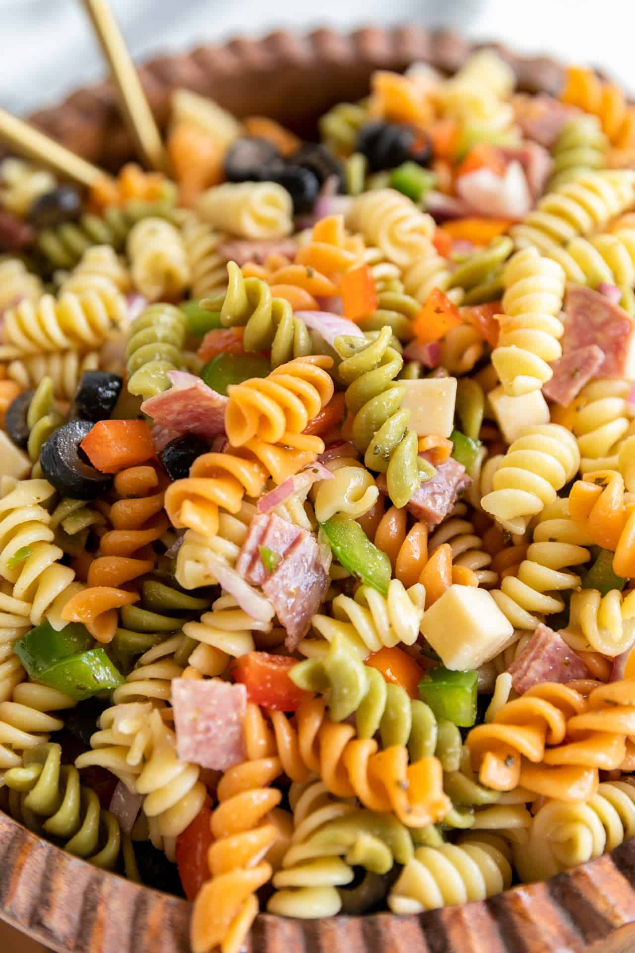 up close ready to serve Antipasto Pasta Salad up close with gold serving spoons in a wood bowl