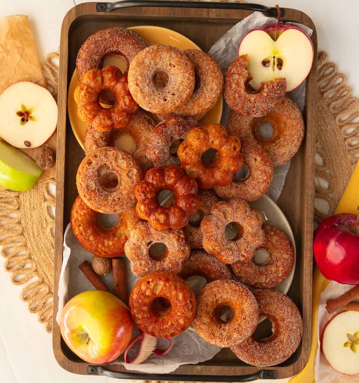 Tray of baked apple cider donuts in various shapes with cinnamon sugar coating and fresh apples
